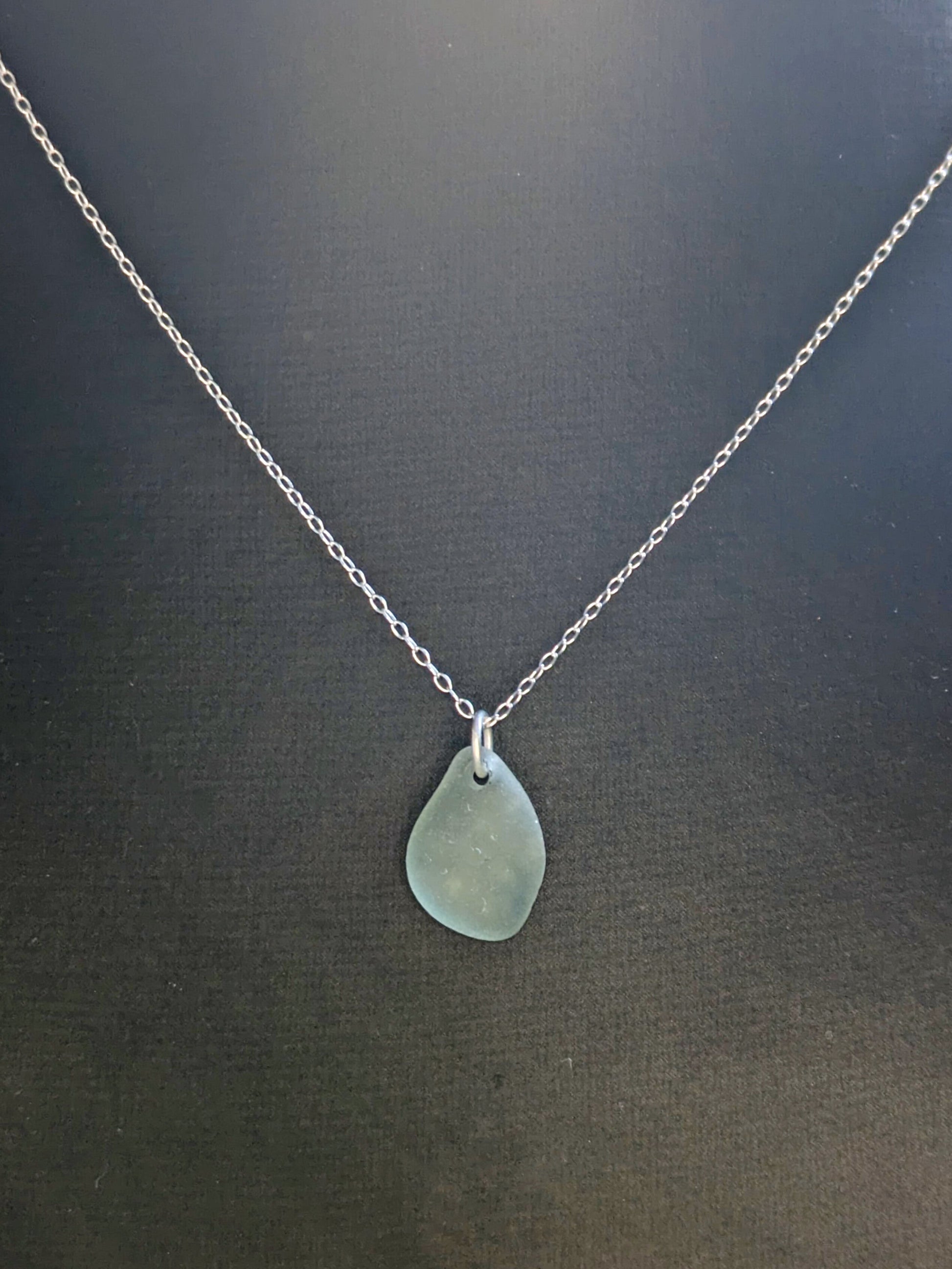 Necklace with a teardrop-shaped sea glass pendant on a dark background